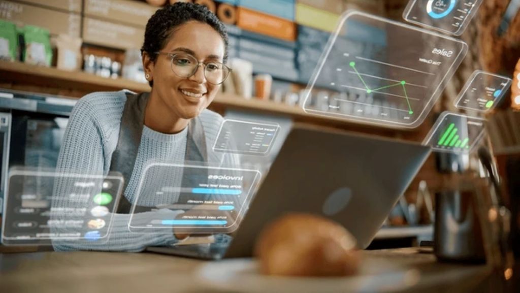 A small business owner smiling at a laptop screen showing cloud dashboard analytics in a modern cafe setting.